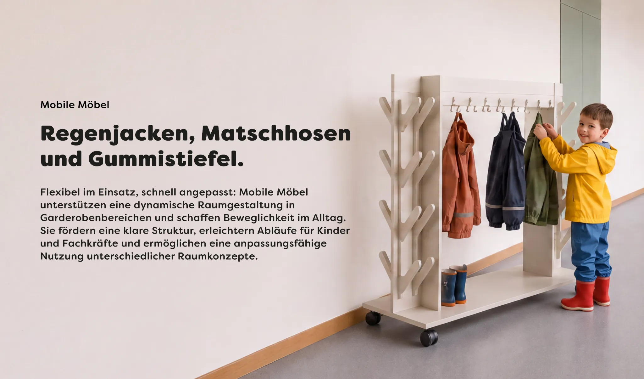 Kind an einem mobilen Garderobenwagen für Kita und Kindergarten mit Kleiderhaken, Ablage und Rollen für flexibel nutzbare Garderobenbereiche.
